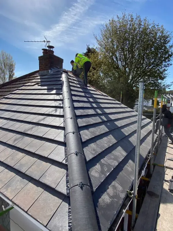 Roofer fitting slate tiles with lead ridge flashing on a Bath roof